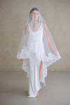 Model wears a lace wedding veil, drop veil with lace trim.