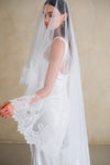 Model wears a lace wedding veil, drop veil with lace trim.