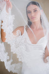 Model wears a lace wedding veil, drop veil with lace trim.