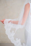 Model wears a lace wedding veil, drop veil with lace trim.